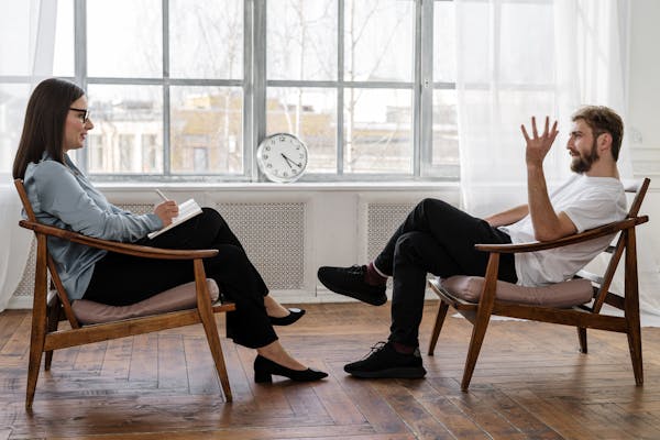 Person in Black Pants and Black Shoes Sitting on Brown Wooden Chair